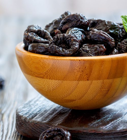 Dried black plums in bowl on wooden table, selective focus.