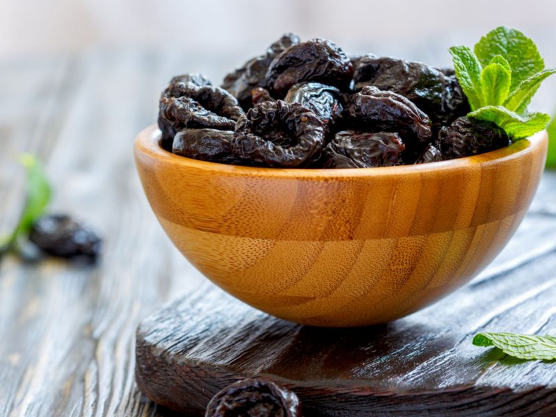 Dried black plums in bowl on wooden table, selective focus.