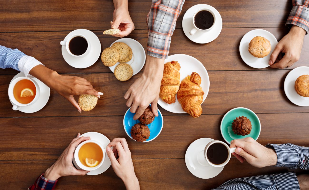 Picture of people's hands on wooden table with croissants and cups of coffee.