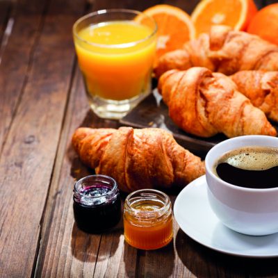breakfast with cup of coffee, croissants, orange juice and fruit jam on wooden table